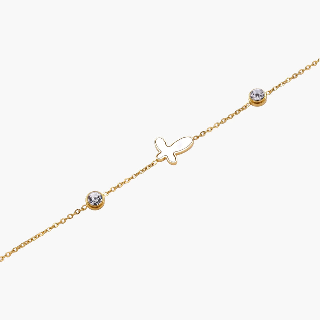 Gold chain bracelet with white mother of pearl butterfly pendant and two bezel-set crystals on cream background
