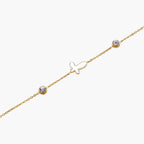 Gold chain bracelet with white mother of pearl butterfly pendant and two bezel-set crystals on cream background