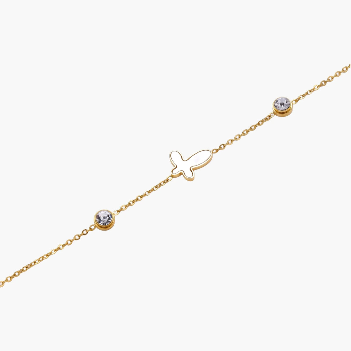 Gold chain bracelet with white mother of pearl butterfly pendant and two bezel-set crystals on cream background