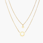 Gold layered necklace set with sunburst and smiley face pendants on delicate chains against white background.