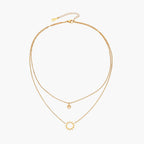 Gold layered necklace set with sunburst and smiley face pendants on delicate chains against white background.