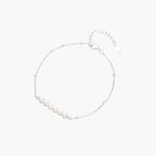 Delicate rhodium-plated silver chain bracelet with row of small baroque pearls centered on white background.