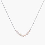 Delicate sterling silver chain necklace with small freshwater pearls arranged in a curved smile arc on cream background.