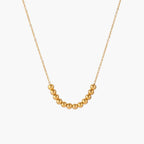 Delicate gold-plated necklace with graduated spherical beads forming gentle smile curve on beige background
