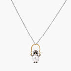 Whimsical owl pendant holding a white pearl on a gold swing, rhodium-plated silver chain on cream background.