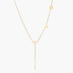 Gold Y-shaped necklace with L-O-V-E letter charms and vertical bar pendant on delicate chain against cream background