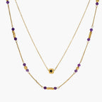 Two layered gold-tone necklaces with purple stone beads and star pendant against cream background.