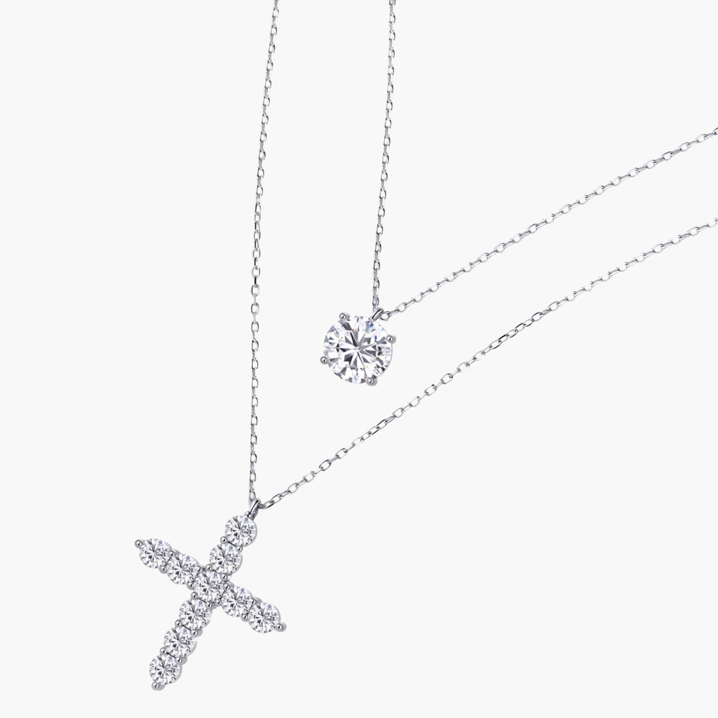 Two delicate sterling silver necklaces with moissanite stones - one solitaire pendant and one cross pendant on white background.