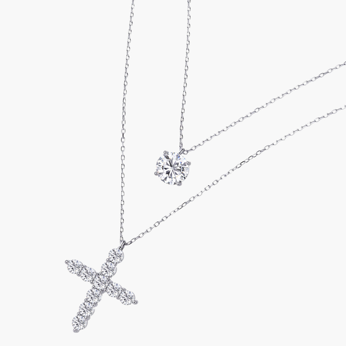 Two delicate sterling silver necklaces with moissanite stones - one solitaire pendant and one cross pendant on white background.